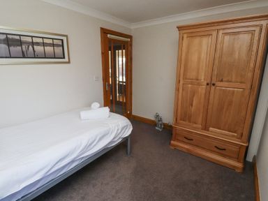 A bedroom with a single bed with white linens a wooden wardrobe a door with glass panels and a framed photo on the wall at Tree Corner in Beadnell