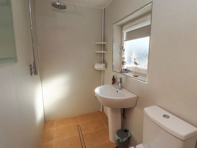 A bathroom with a shower, pedestal sink, toilet, window with decorations, and a small trash bin at Tree Corner in Beadnell