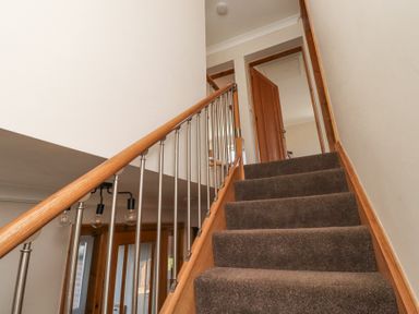 A carpeted staircase with wooden handrail and metal balusters leading to an open doorway at Tree Corner in Beadnell