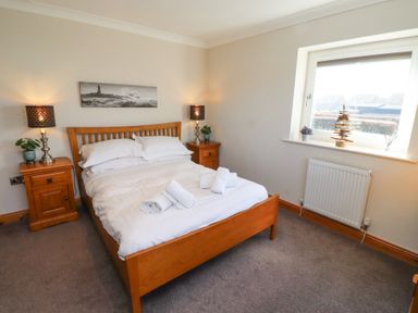 A bedroom with a wooden bed white bedding two bedside tables with lamps and a window at Tree Corner in Beadnell