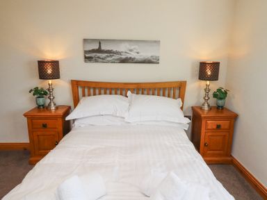 A bedroom with a bed between two wooden nightstands each with a lamp and plant at Tree Corner in Beadnell