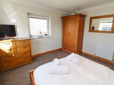 A bedroom with a wooden dresser holding a TV a wooden wardrobe a bed with rolled white towels and a wall mirror at Tree Corner in Beadnell