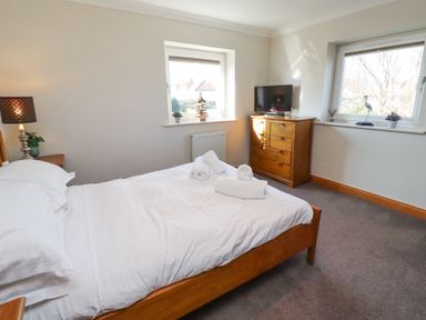 A bedroom with a wooden bed and dresser a TV and two windows at Tree Corner in Beadnell