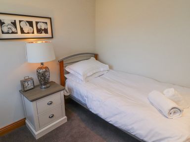 A bedroom with a single bed white bedding a nightstand lamp and clock and black and white flower pictures on the wall at Tree Corner in Beadnell