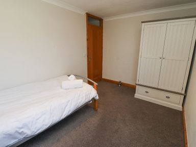 A bedroom with a single bed with white sheets and folded towels a wooden door and a white wardrobe at Tree Corner in Beadnell