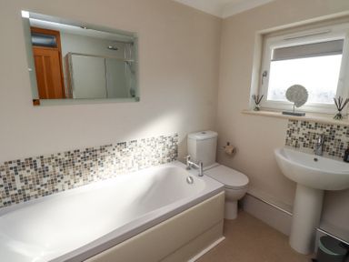 A bathroom with a bathtub, toilet, sink, mirror, and window at Tree Corner in Beadnell