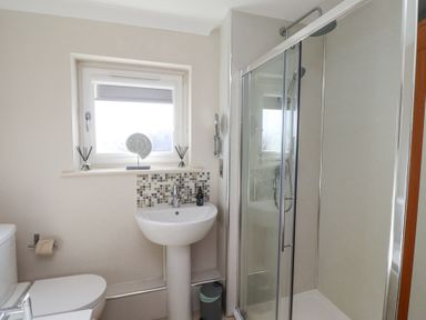 A bathroom with a toilet sink shower and a window at Tree Corner in Beadnell