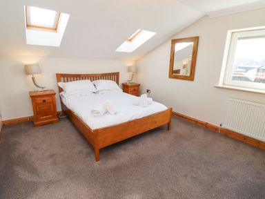 A bedroom with a wooden bed and bedside tables with lamps under skylights and a window at Tree Corner in Beadnell