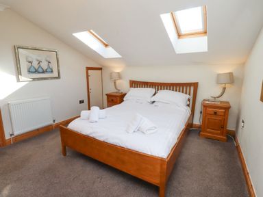 A bedroom with a wooden bed a white duvet two bedside tables with lamps and skylight windows at Tree Corner in Beadnell