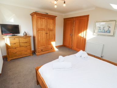 A bedroom with a bed and towels on it a wooden wardrobe and dresser with a television and framed picture on the wall at Tree Corner in Beadnell
