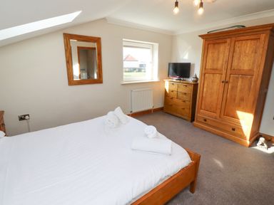 A bedroom with a bed, wooden dresser, wardrobe, mirror, window, and television at Tree Corner in Beadnell