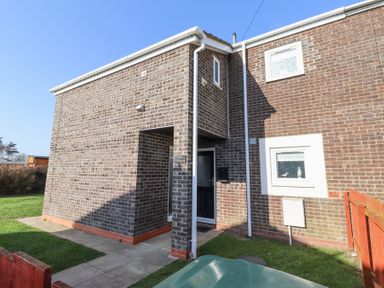 The exterior of a brick house with a doorway and two windows and a small lawn at Tree Corner in Beadnell