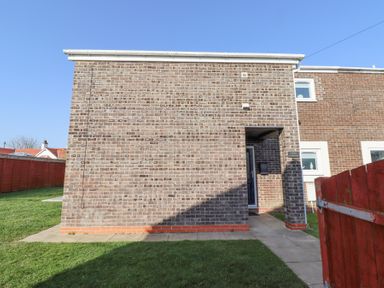 The exterior of a brick house with a small covered entrance and a red wooden fence at Tree Corner in Beadnell