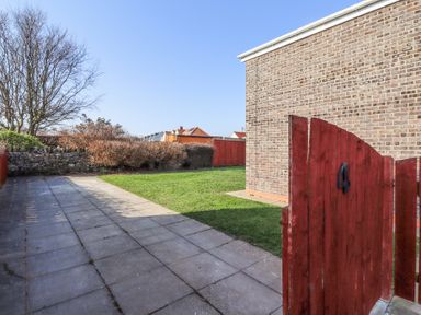 A garden with a grass lawn a tiled pathway and a red wooden gate with the number 4 at Tree Corner in Beadnell