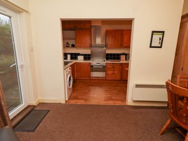 A kitchen with wooden cabinets and a washing machine at Wayside Cottage in Newton-by-the-Sea