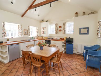 A kitchen with wooden table and chairs a vase with flowers blue armchairs and windows with patterned curtains at Wynding Down in Bamburgh