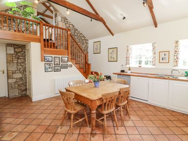 A kitchen dining area with a wooden table and chairs under exposed wooden beams and stone walls at Wynding Down in Bamburgh