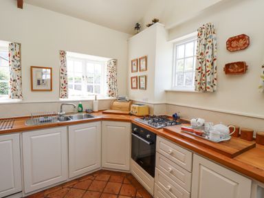 A kitchen with white cabinets a wooden countertop a gas stove a sink and patterned curtains at Wynding Down in Bamburgh