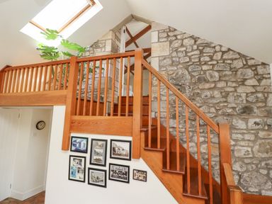 An indoor staircase with wooden railing and stone wall with framed pictures on the lower white wall at Wynding Down in Bamburgh