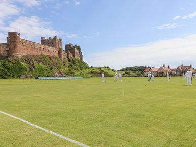 People playing croquet on a grass field near a large stone castle and houses at Wynding Down in Bamburgh