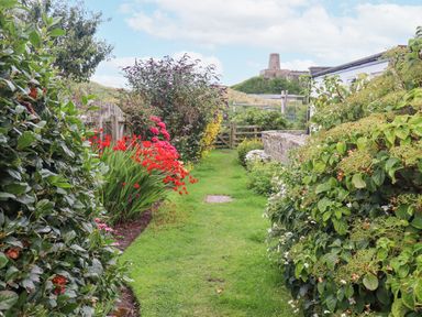 A garden path with green grass and flowering plants along stone wall and wooden fence at Wynding Down in Bamburgh