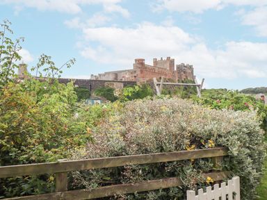 A garden with flowering bushes and a wooden fence with a castle in the background at Wynding Down in Bamburgh