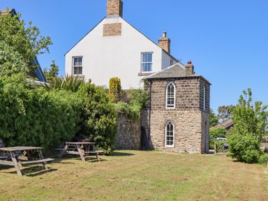 A yard with wooden picnic tables and a stone building with arched windows at The Lookout Embleton