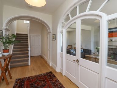 A hallway with wooden flooring a carpet a potted plant on a small wooden table stairs and white double doors leading to a living room at The Lookout (Embleton) in Embleton