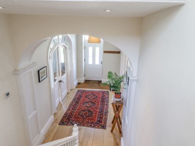 A hallway with a red patterned rug a wooden floor an arched doorway a small wooden table with a potted plant and a white front door at The Lookout (Embleton) in Embleton