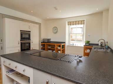 A kitchen with a central island stove white cabinets wall ovens and a window at The Lookout Embleton