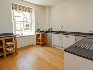 A kitchen with wooden floor white cabinets black countertops a window and wooden shelves at The Lookout Embleton