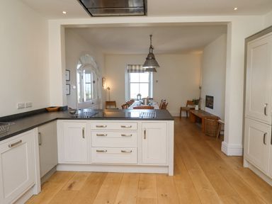 A kitchen with white cabinets and black countertops opening to a dining area with a wooden table and chairs at The Lookout Embleton