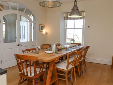A dining room with a wooden table and chairs set for a meal near a window at The Lookout Embleton