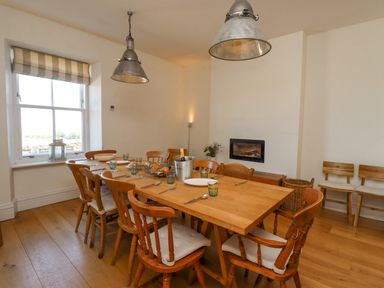 A dining room with a wooden table set with plates glasses and cutlery and wooden chairs around a window at The Lookout Embleton