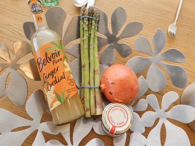 A bottle of ginger cordial, a bundle of asparagus, a pomegranate, and a jar of honey on a metal floral tray on a wooden table at The Lookout in Embleton