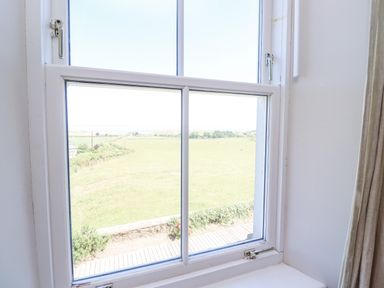 A window with white frame looking out to a green field and clear sky at The Lookout Embleton