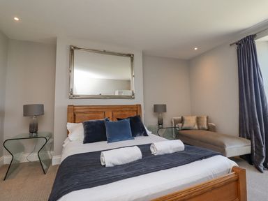 A bedroom with a wooden bed with cushions and towels a glass bedside table with lamp and a chaise lounge at The Lookout (Embleton) in Embleton