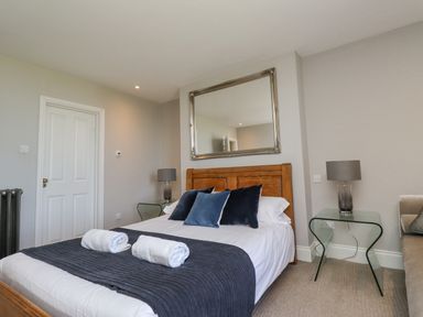 A bedroom with a wooden bed frame glass side tables lamps and a large mirror at The Lookout Embleton
