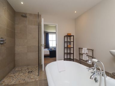 A bathroom with a bathtub a walk-in shower a shelving unit and a towel rack at The Lookout Embleton