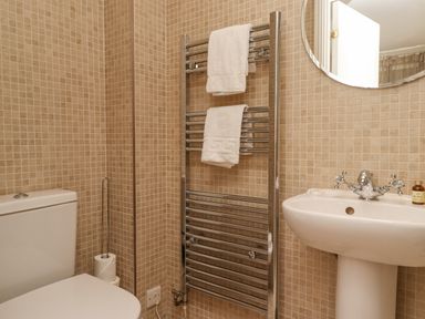 A bathroom with a toilet, pedestal sink, towel rack with two white towels and beige tiled walls at The Lookout Embleton