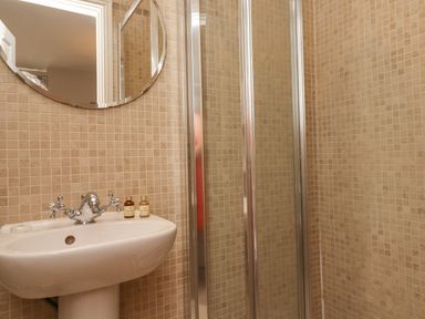 A bathroom with a white pedestal sink a round mirror and a glass shower enclosure at The Lookout Embleton