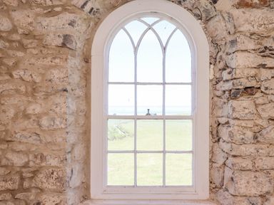 A stone wall with an arched window showing a green field outside at The Lookout Embleton