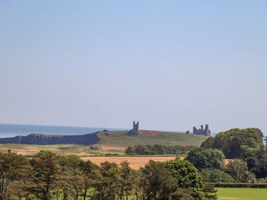 A grassy hill with castle ruins near the coast with trees and fields in the foreground at The Lookout (Embleton) in Embleton
