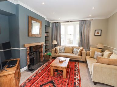 A living room with two beige sofas a wooden coffee table a red patterned rug and a TV on a wooden cabinet at The Hollies in Bamburgh