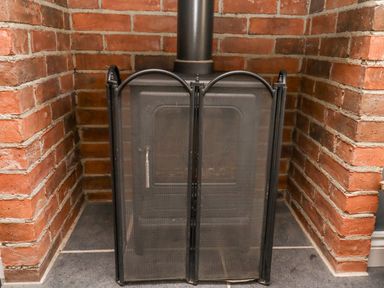 A black wood stove with a mesh fire screen in front set in a brick alcove at The Hollies in Bamburgh
