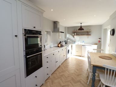 A kitchen with white cabinets a wooden dining table and chairs a double oven and washing machine at The Hollies in Bamburgh