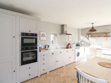 A kitchen with white cabinets double oven washing machine wooden table and chairs at The Hollies in Bamburgh