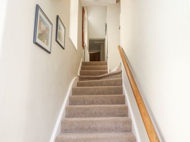 A carpeted staircase with wooden handrail and framed pictures on the wall at The Hollies in Bamburgh