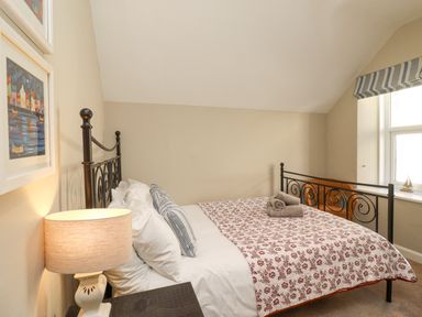 A bedroom with a patterned bedspread on a metal bed frame and a table lamp on a bedside table at The Hollies in Bamburgh