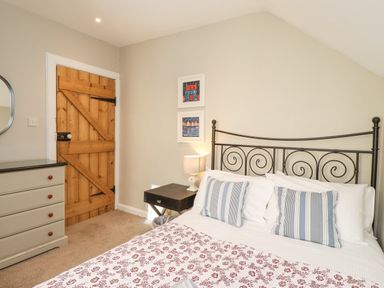 A bedroom with a bed and striped pillows a wooden door a dresser and two framed pictures on the wall at The Hollies in Bamburgh
